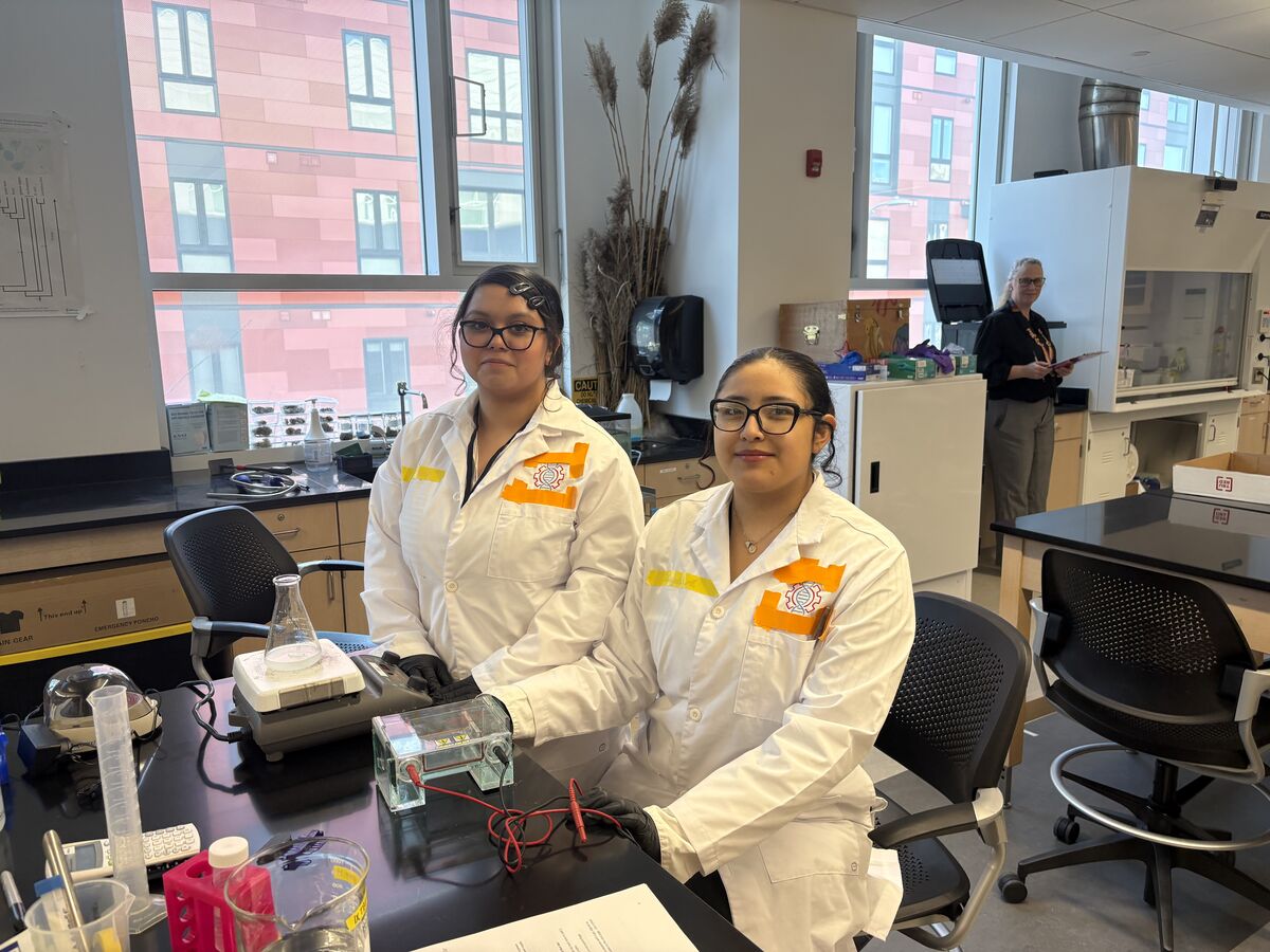 Two young women in lab coats work with scientific equipment in a laboratory.
