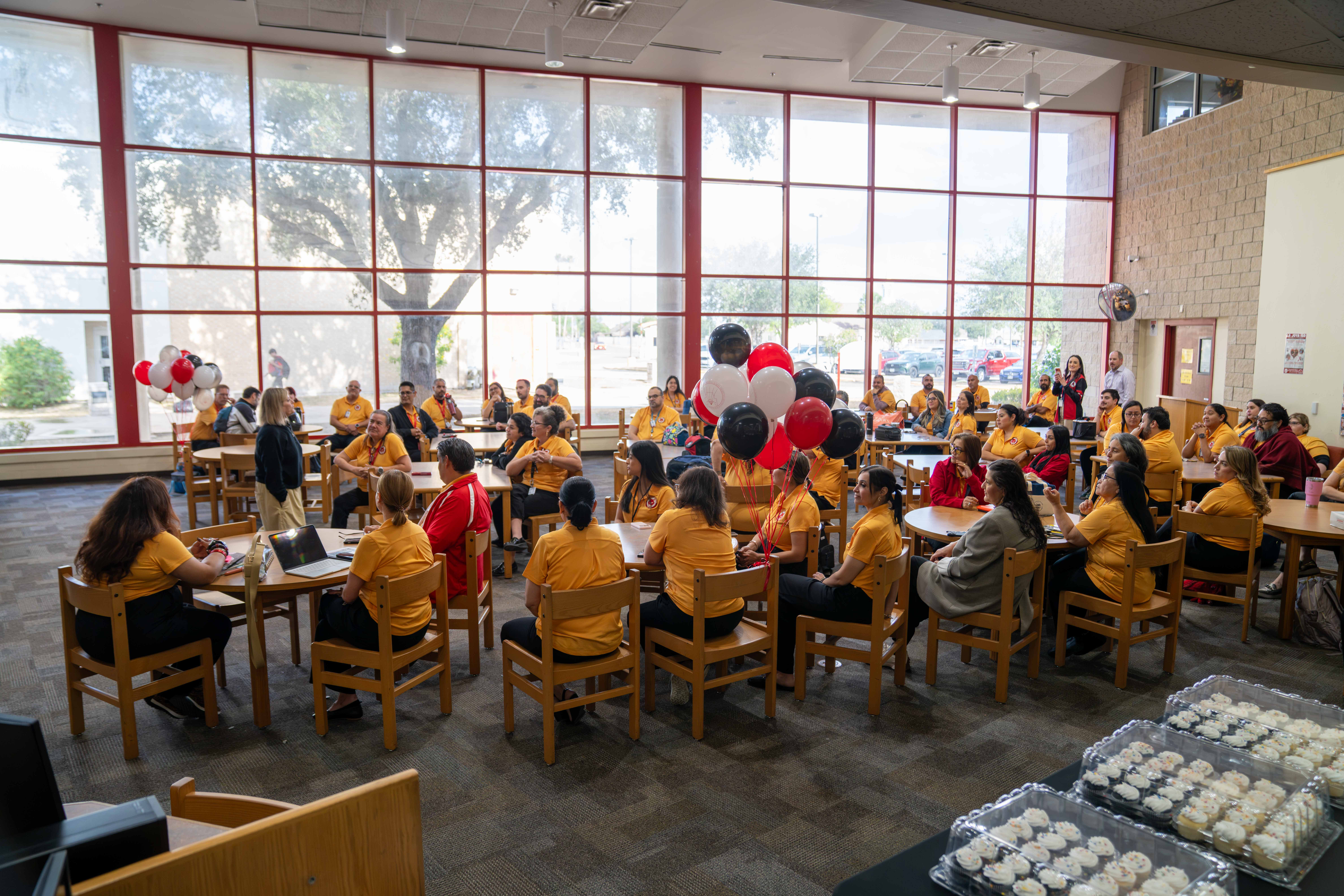 A large group of people in yellow shirts gathers in a brightly lit room with tall windows.