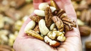 A hand holds a mix of assorted nuts, including pecans and almonds.