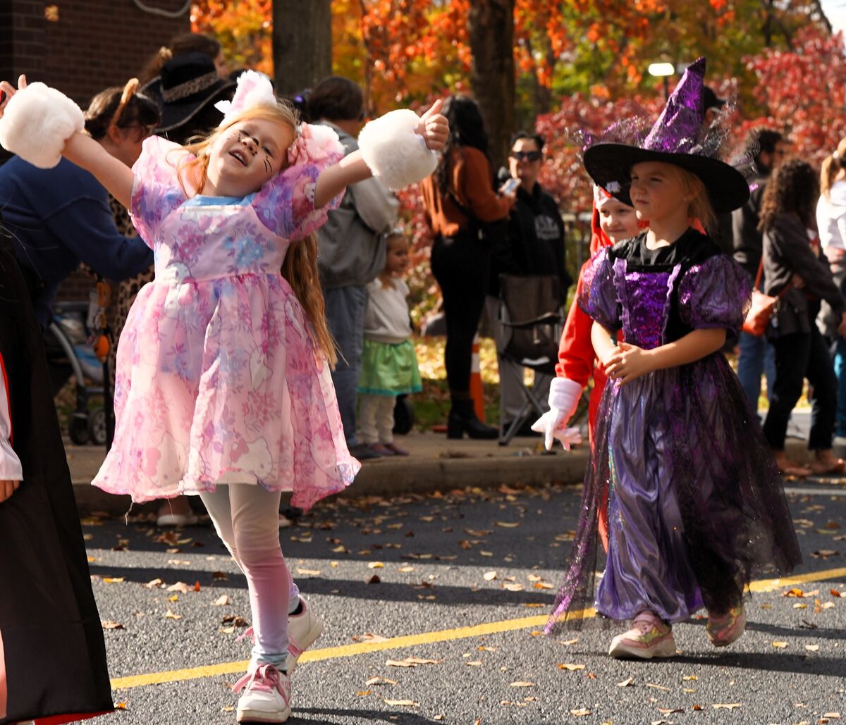 Two children in Halloween costumes walk down a street during an outdoor event.