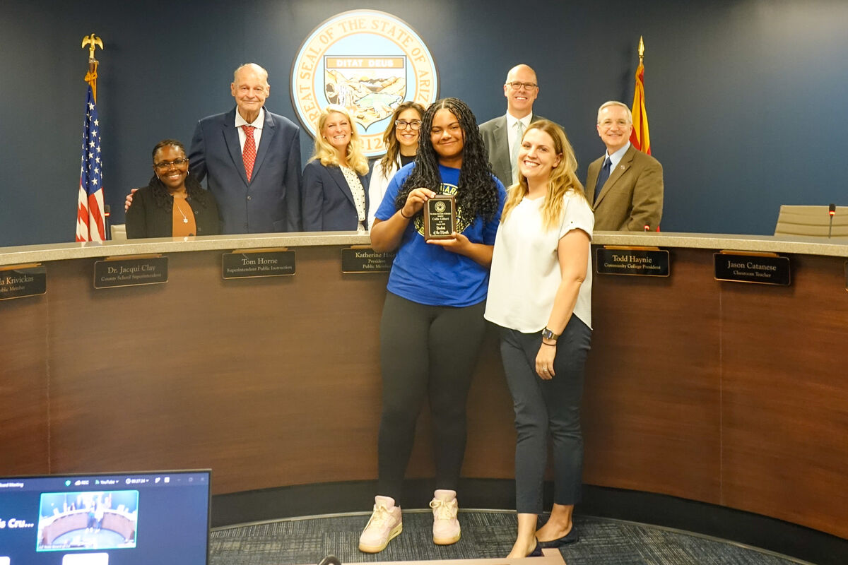 A young woman receives a plaque from two smiling women in front of a group of officials.