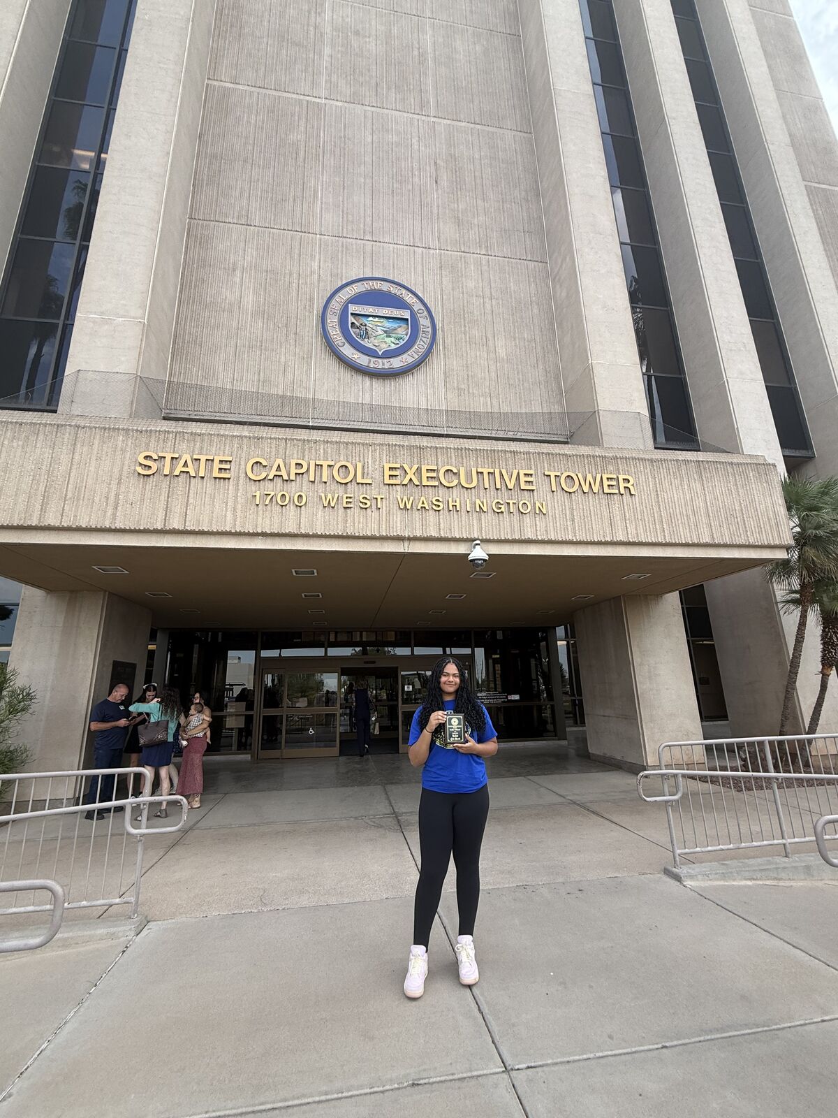 A young woman holds a plaque in front of the State Capitol Executive Tower at 1700 West Washington.