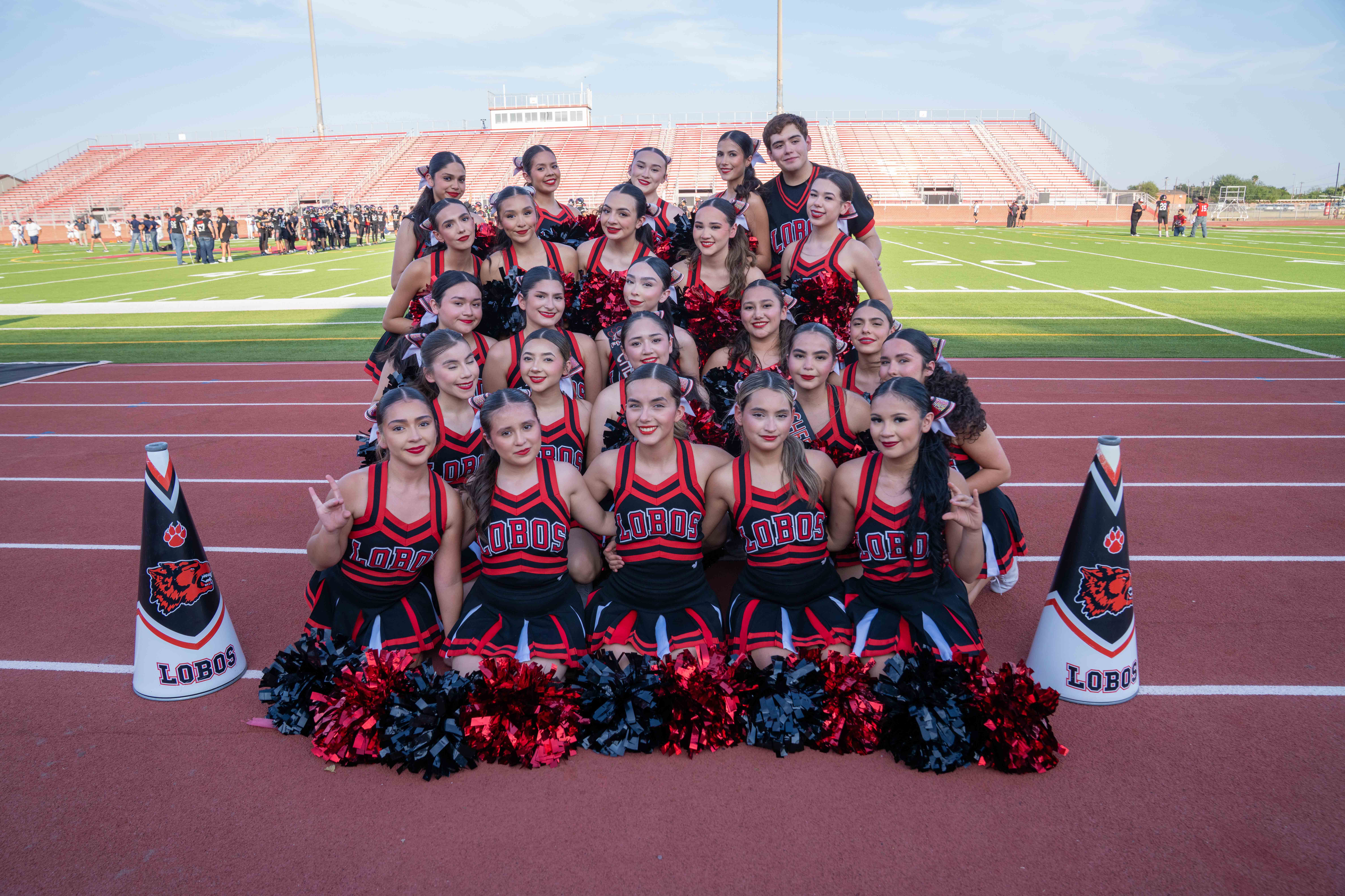 A high school cheerleading team poses for a group photo on a running track, wearing red and black uniforms that read "LOBOS".