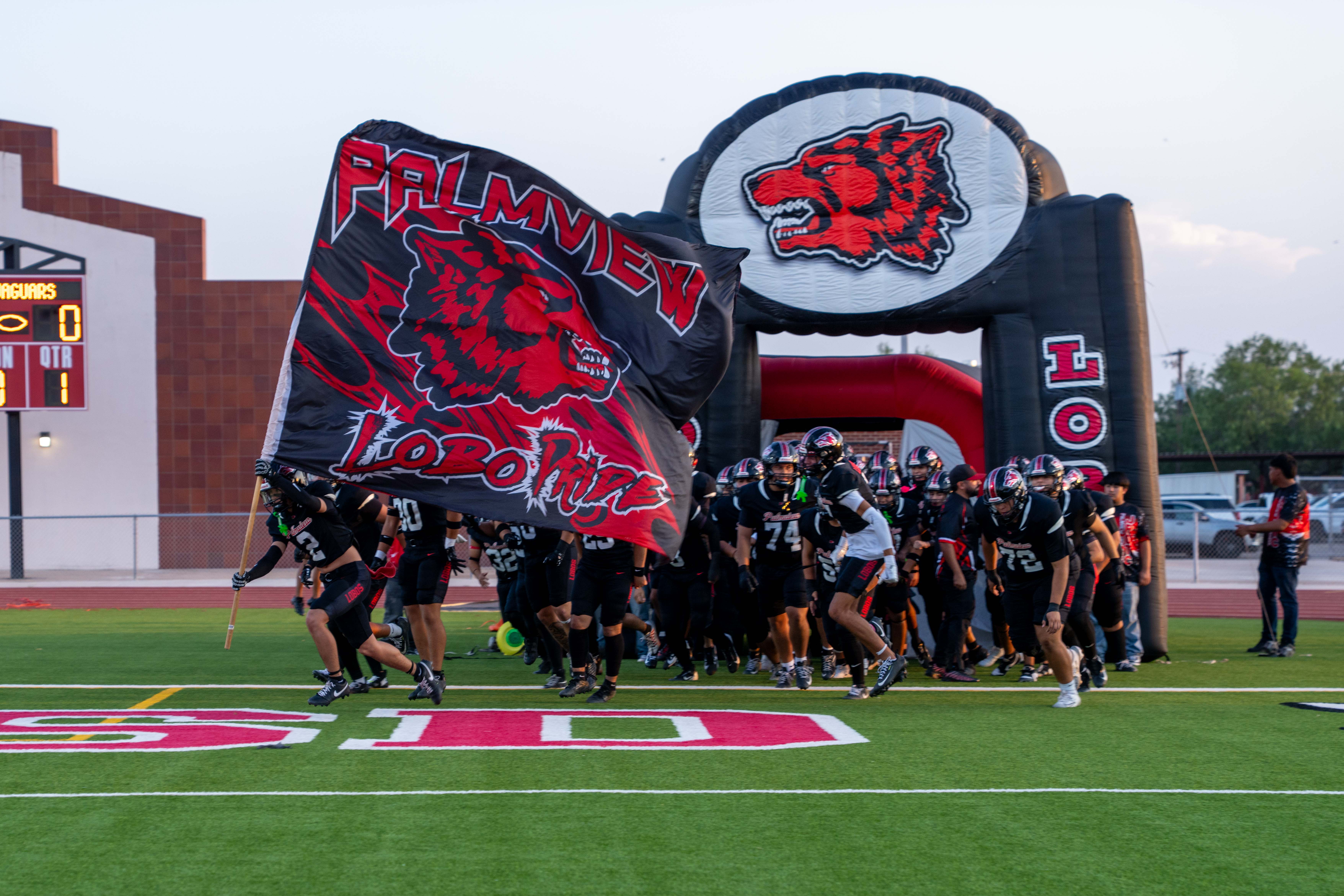 Football players run onto field with the PHS Lobo flag. 