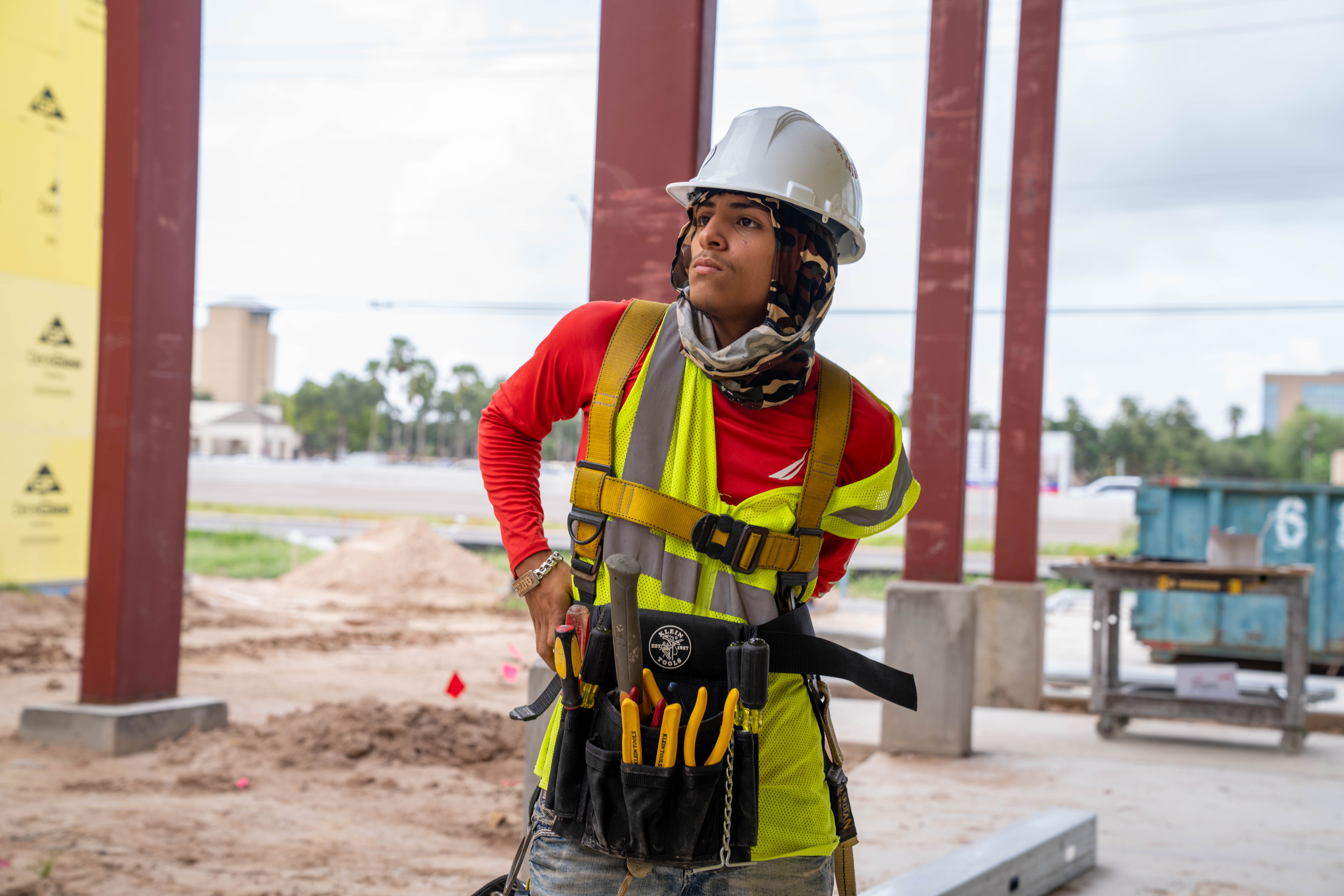 A construction worker wearing a hard hat and safety vest stands on a job site.