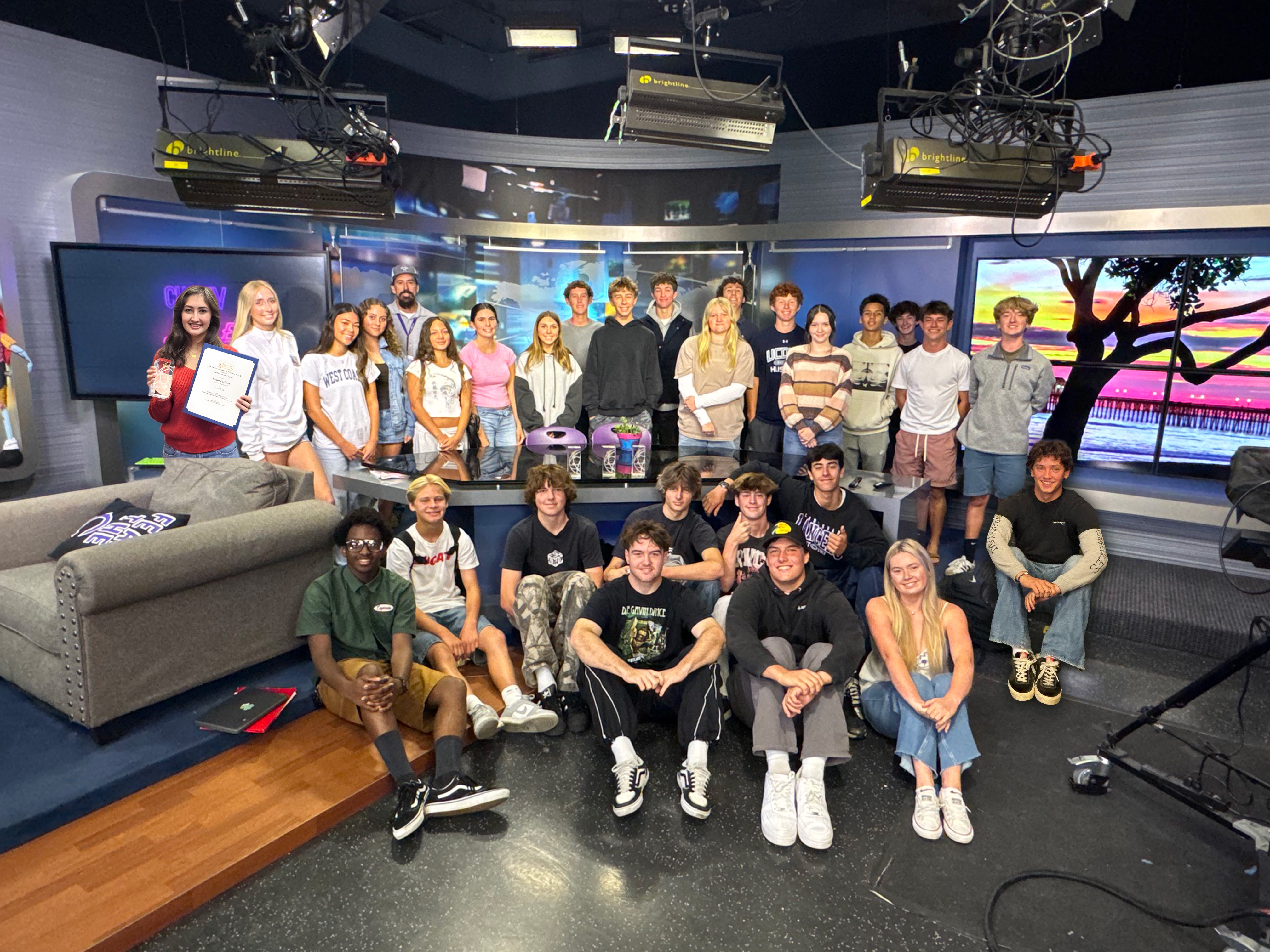 A group of students poses for a photo in a television studio with a scenic backdrop.