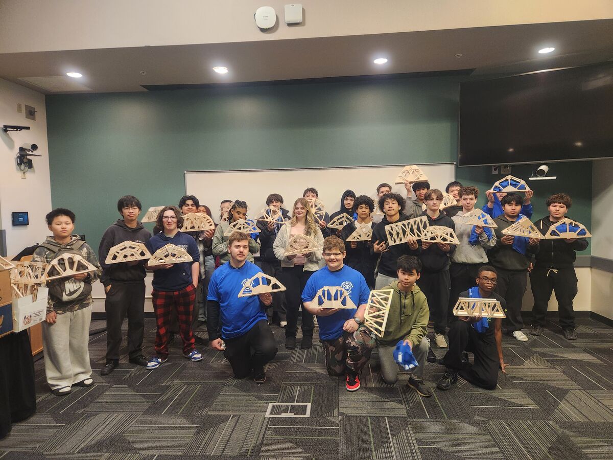A diverse group of students proudly displays their handmade wooden bridge models.