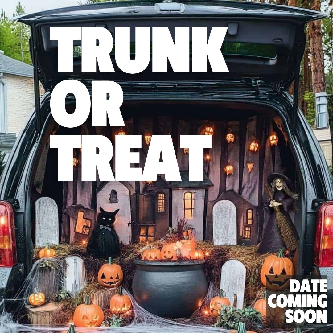 A car trunk is decorated for Halloween with miniature houses, pumpkins, a black cat, and a witch figure.