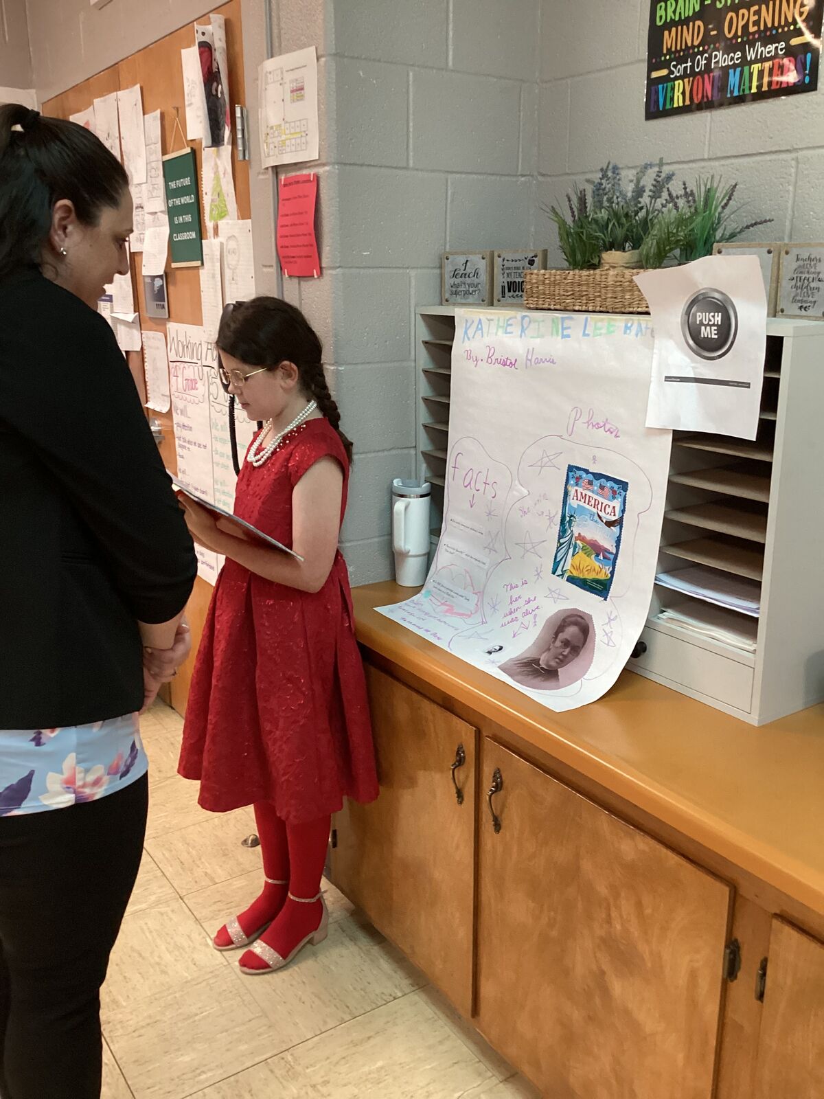 A young person in a red dress and pearls reads a report about Katherine Lee Bates.
