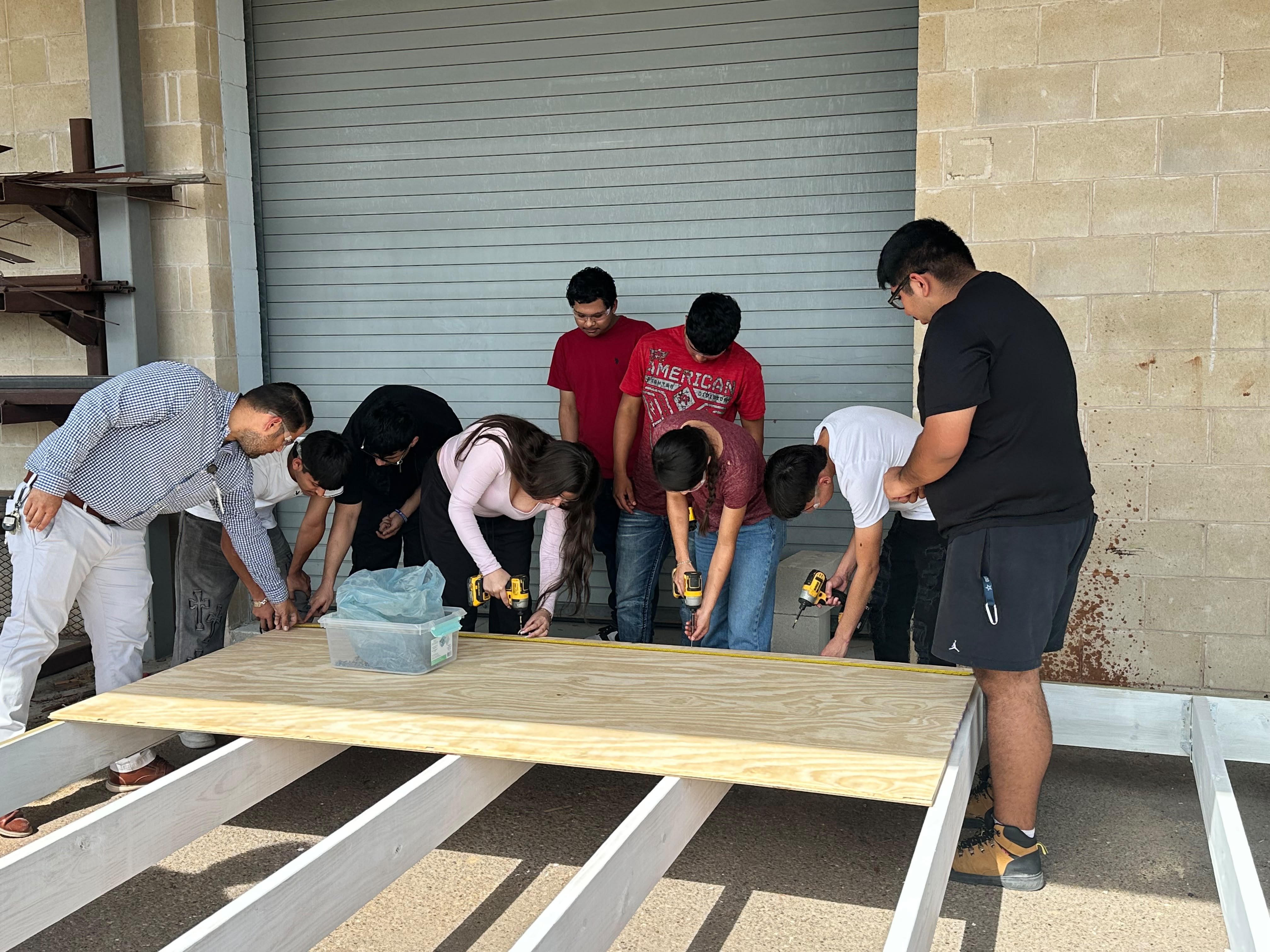 A group of people work together to build a wooden structure outside a building.