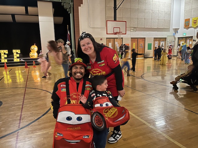 A family dressed in Lightning McQueen costumes poses together on a gymnasium floor during an event.