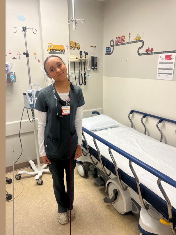 A healthcare worker in dark green scrubs smiles in a pediatric hospital room.
