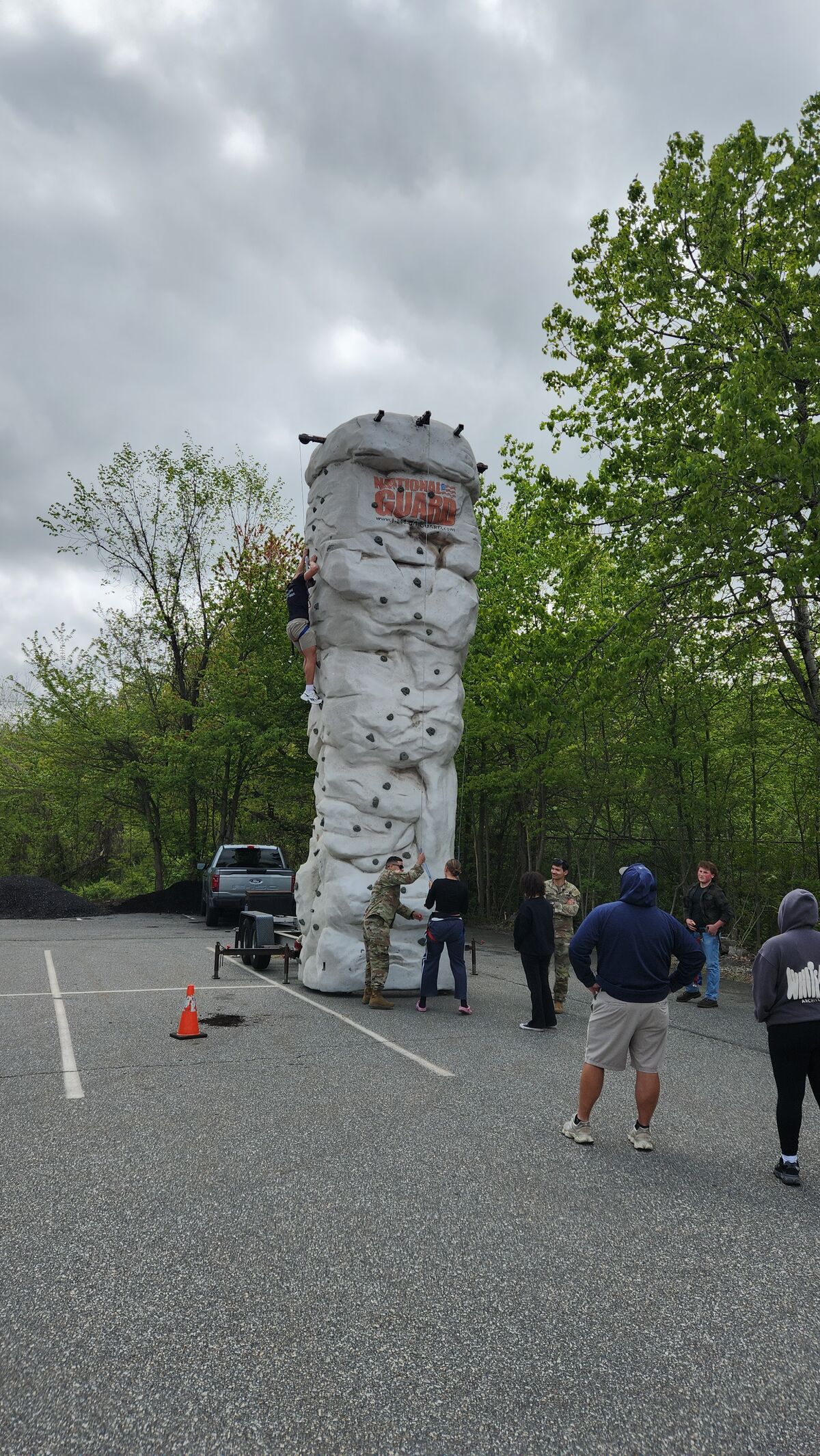 People participate in an outdoor climbing activity on a portable rock wall.