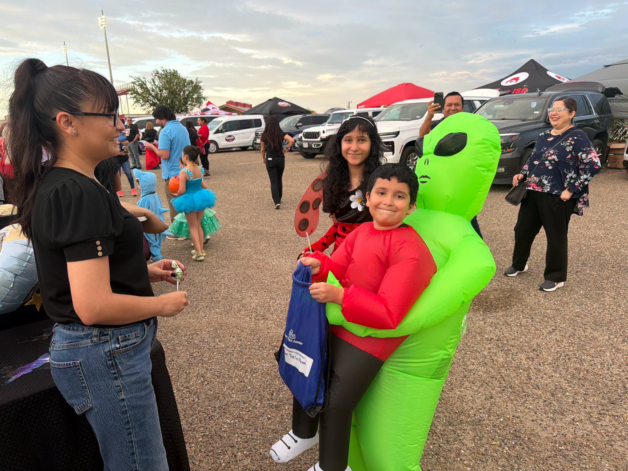 A child in an inflatable green alien costume collects candy from a woman.