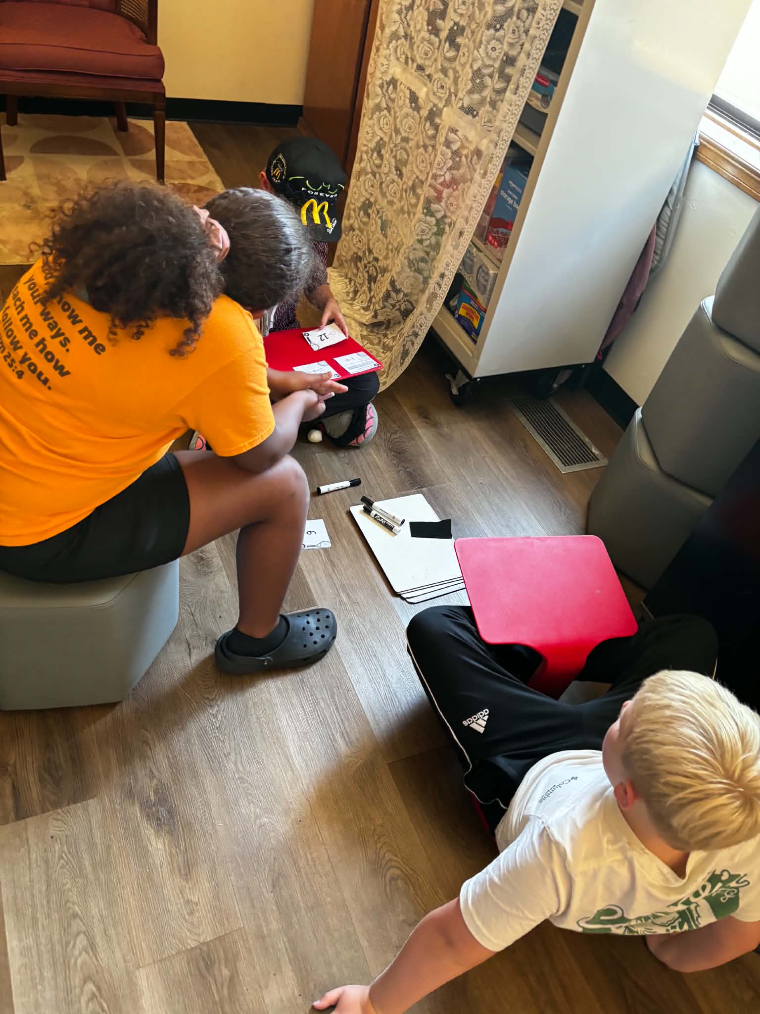 Four children sit on a hardwood floor, playing a game together in a brightly lit room.