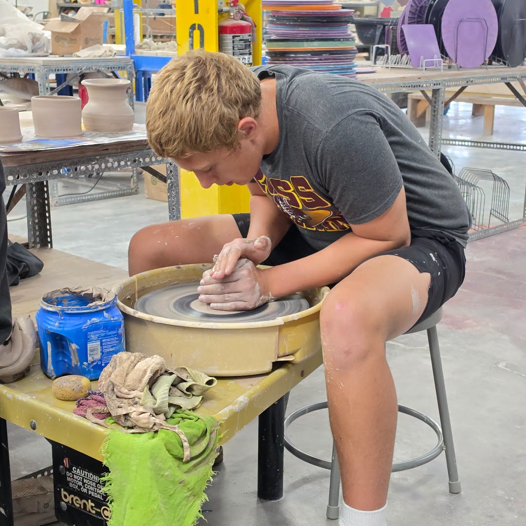 A young person concentrates on shaping clay on a pottery wheel in a workshop.