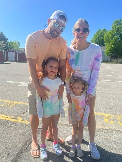 A family poses for a photo, all wearing colorful tie-dye shirts.