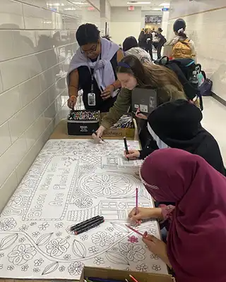 WHS students working on their coloring book wall on a table set up in a hallway.