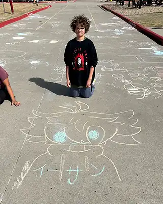 A Draper student posing with his chalk artwork and surrounded by other pieces of art..