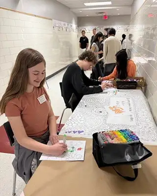 WHS students working on their coloring book wall on a table set up in a hallway.