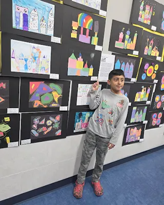 One Kreymer student posing in front of the school created artwork that has been hung on a classroom…