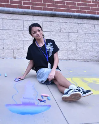 A WEHS student posing with her chalk art outside the school.