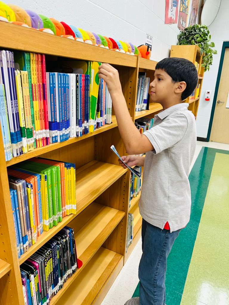 A young boy in a grey shirt and jeans selects a book from a colorful library shelf.