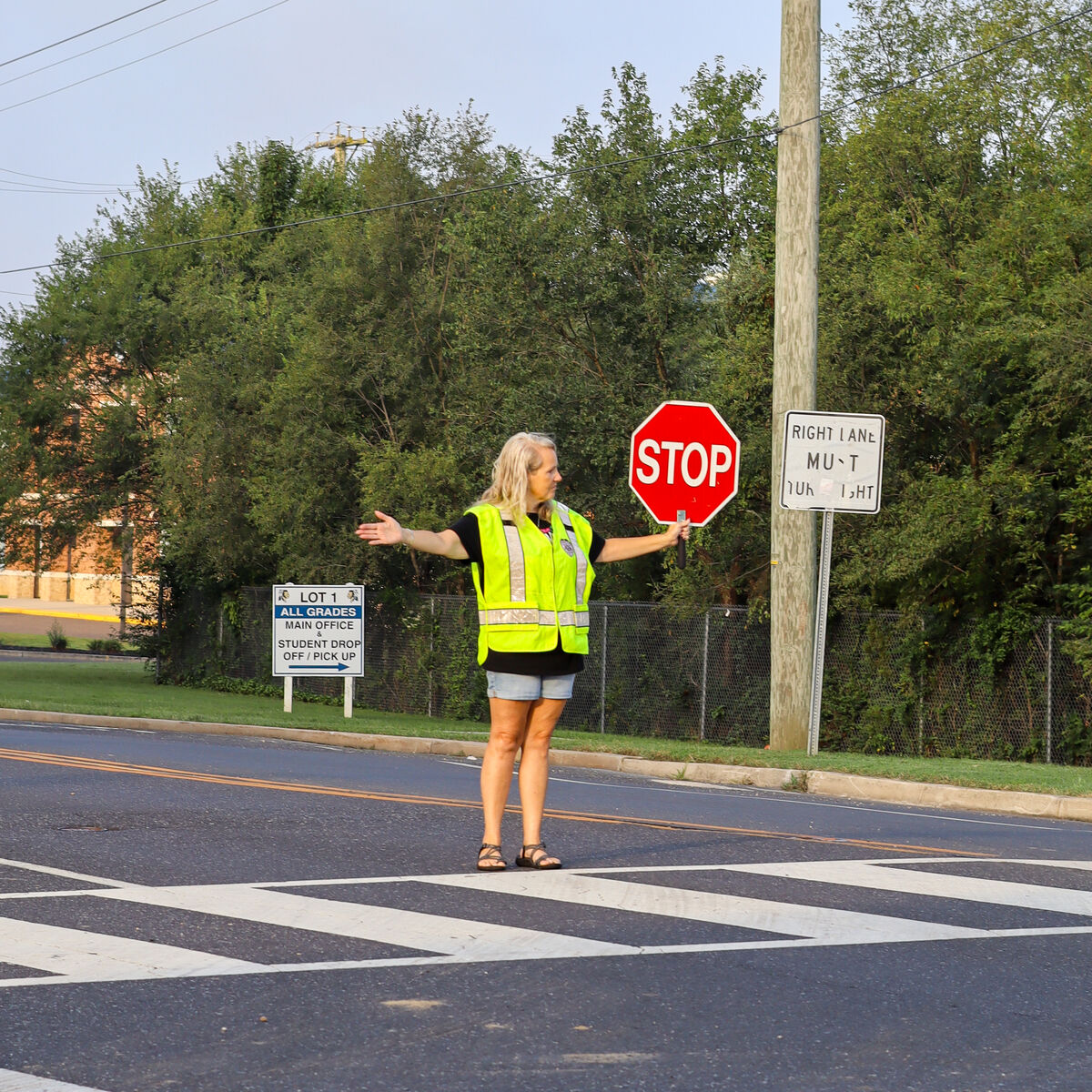 A crossing guard in a high-visibility vest stands in a crosswalk, holding a stop sign.