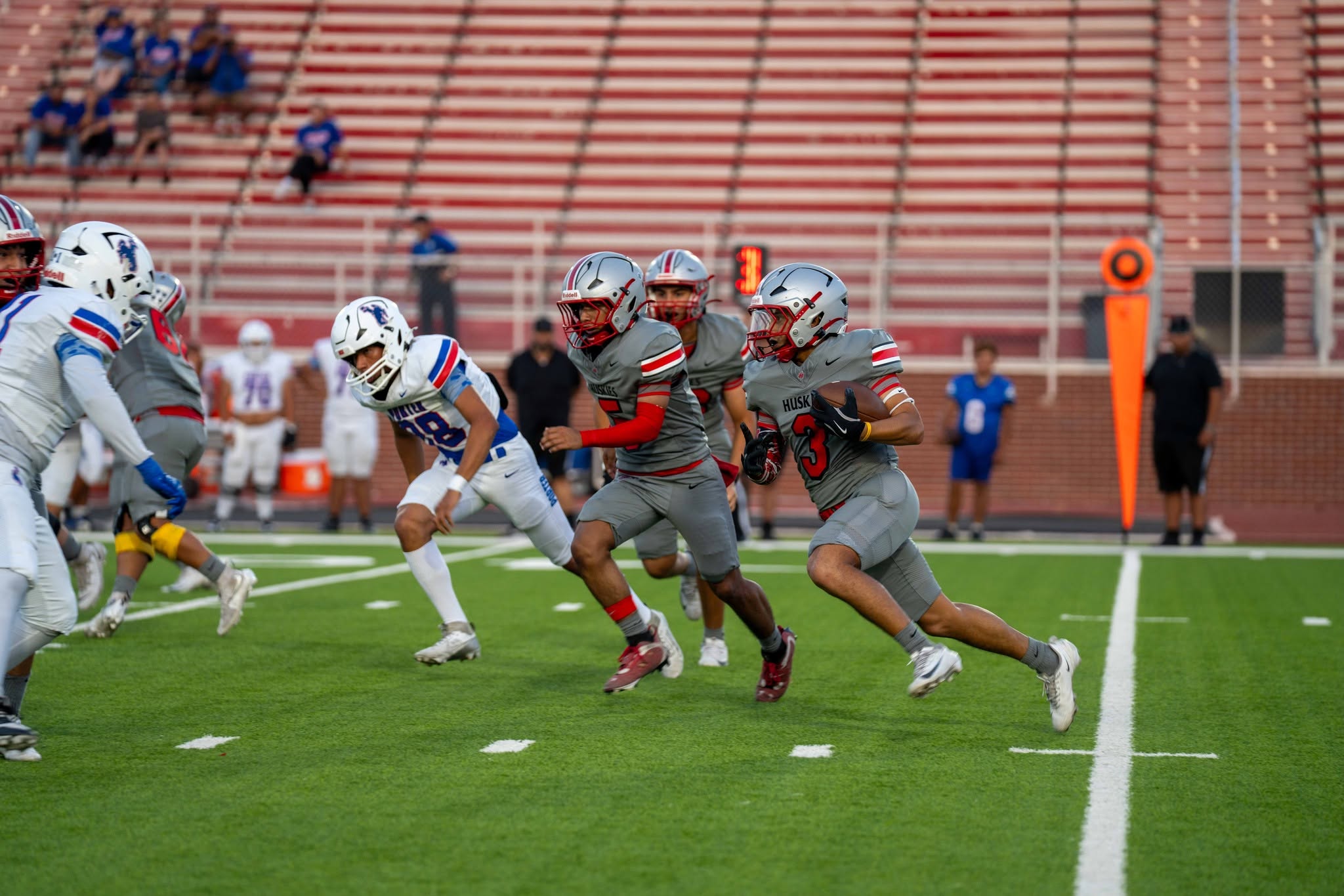 A football player in a grey uniform with the number 3 carries the ball down the field during a game.